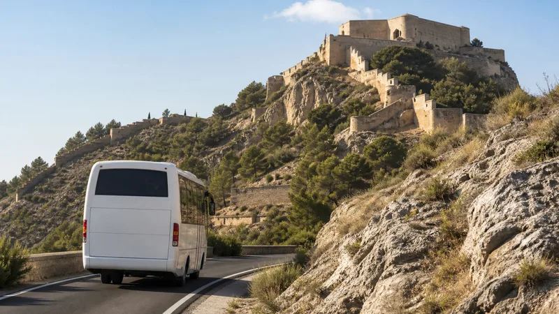 Autobús blanco asciende por una carretera hacia un castillo en la montaña