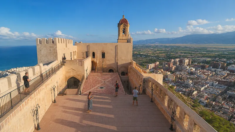 Patio del Castillo de Cullera con visitantes, campanario y paisaje de costa y arrozales