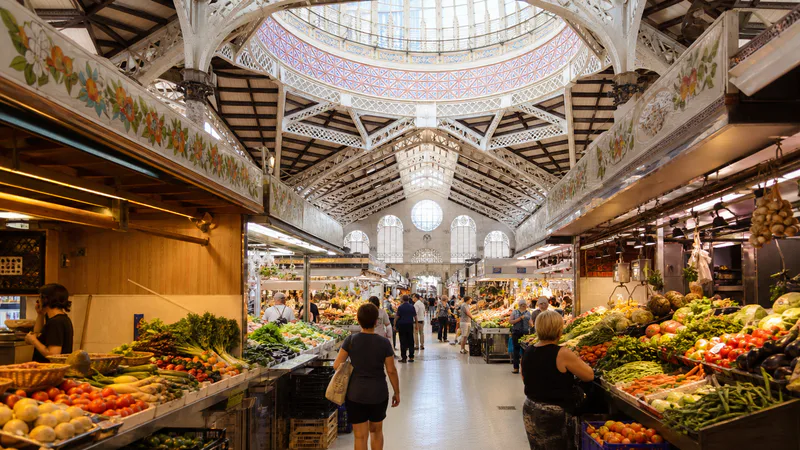 Pasillo de puestos de fruta y verdura bajo la estructura modernista del mercado