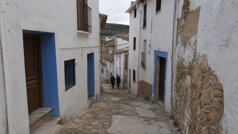 Calle estrecha de un barrio histórico de Chelva con fachadas blancas y detalles azules