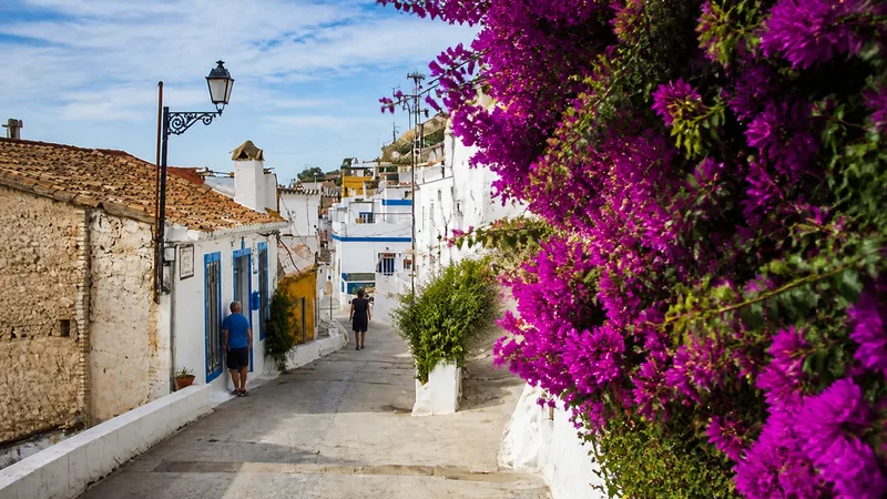 Calle empinada del Barri del Pou con casas blancas, detalles azules y buganvilla