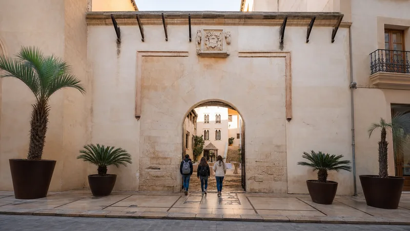 Acceso sobrio de piedra al Palau Ducal de Gandia con visitantes y patio al fondo