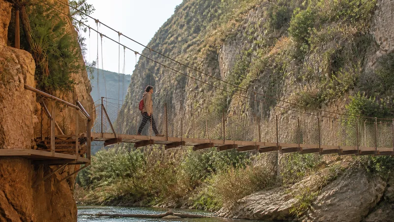 Puente colgante estrecho sobre el río Turia en las Hoces de Chulilla con una persona a escala