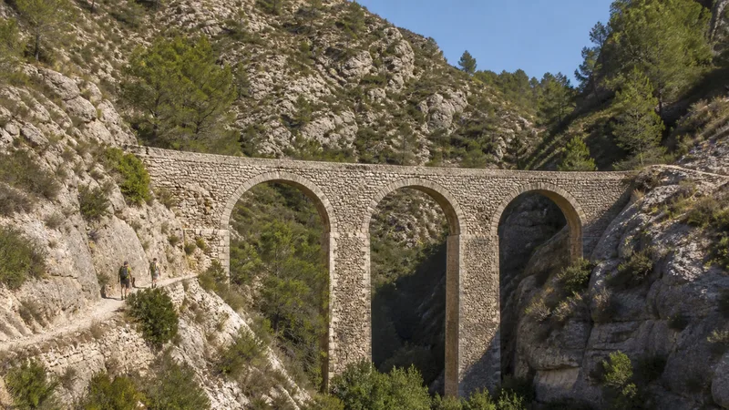 Acueducto de Peña Cortada con tres arcos sobre una garganta y dos senderistas a escala