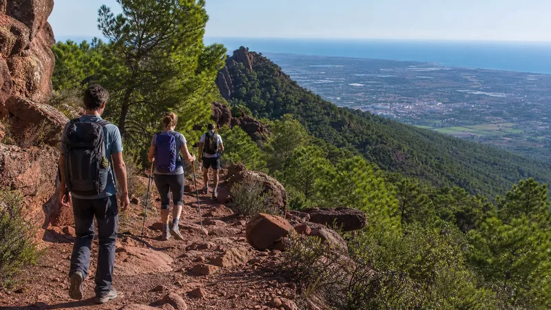 Dos senderistas avanzan por una senda de rodeno en una sierra valenciana con el Mediterráneo al fondo