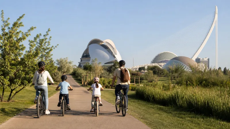 Familia recorriendo en bicicleta el Jardín del Turia con la Ciutat de les Arts i les Ciències al fondo