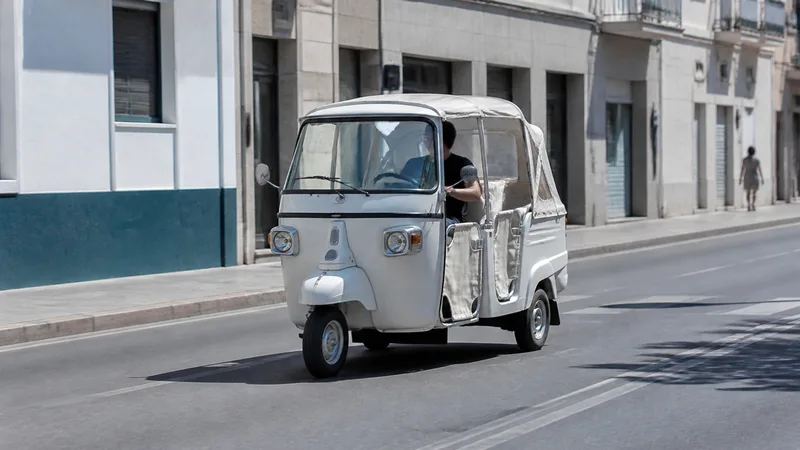 Tuctuc turístico blanco circulando por una calle urbana mediterránea