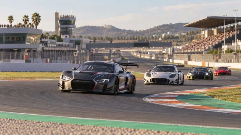 Varios coches GT genéricos atraviesan una curva de un circuito con gradas al fondo.