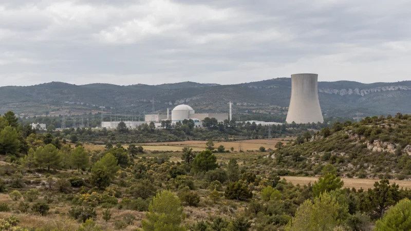 Vista lejana de una instalación energética con torre de refrigeración entre colinas y campos.
