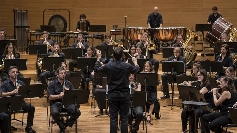 Una banda sinfónica ensaya en una sala de conciertos bajo la dirección de un director