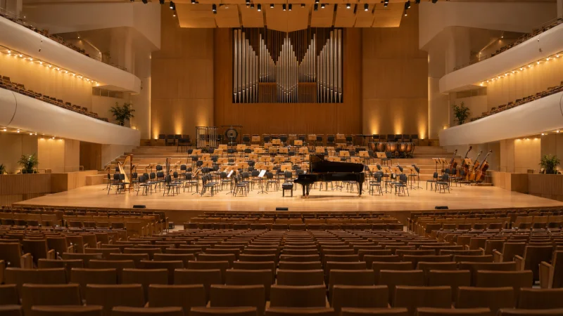 Vista general de una sala de conciertos vacía con piano y atriles en el escenario, imagen ilustrativa generada.